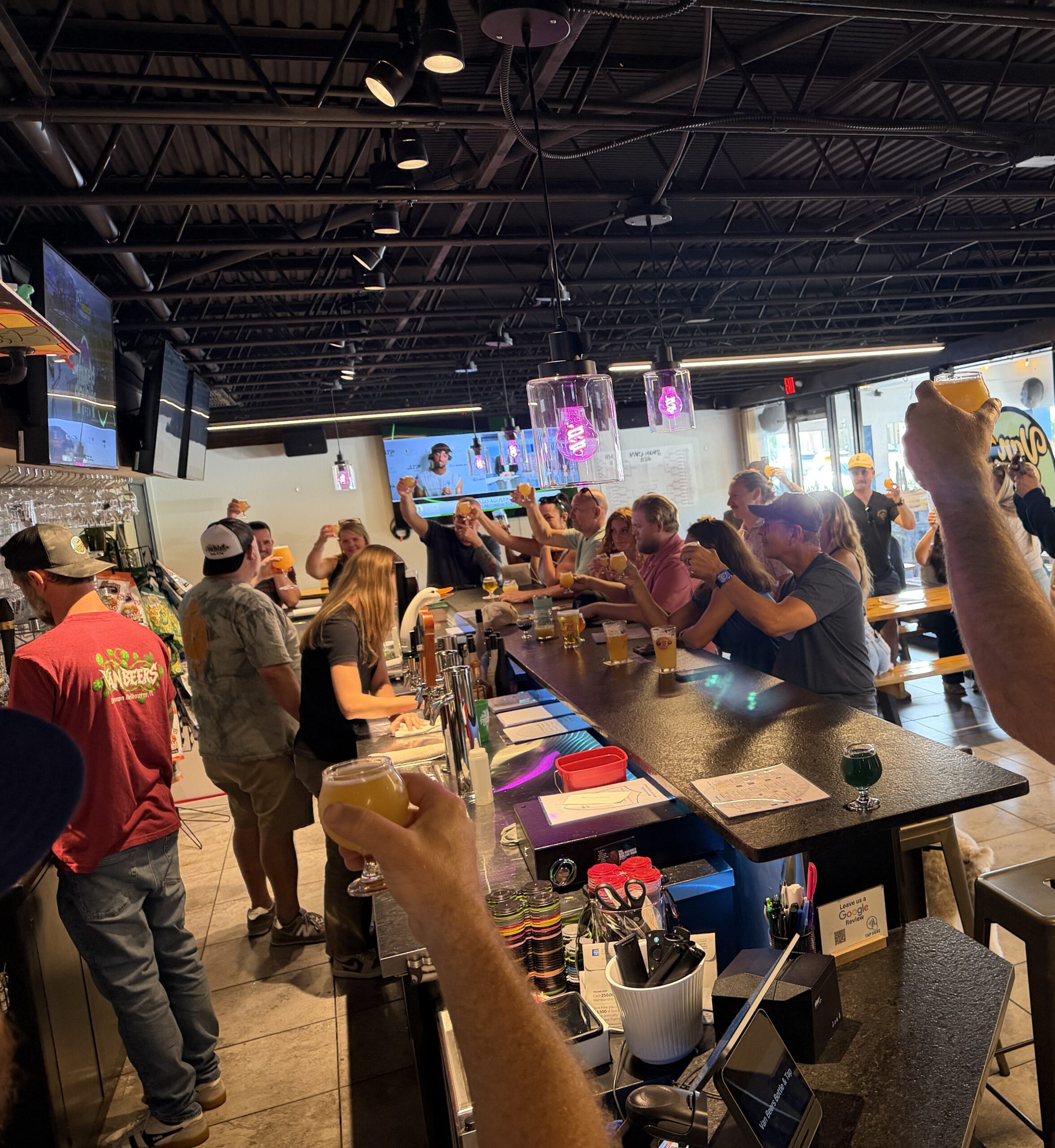 Crowd raising craft beer glasses inside Van Beers Bottle and Tap Room in downtown Melbourne Florida